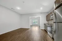 Bright and modern apartment kitchen with sleek stainless steel appliances, wood flooring, and a spacious open layout.