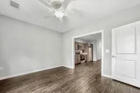 Modern apartment interior with sleek wood flooring leading into a bright kitchen with stainless steel appliances.