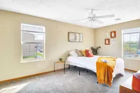 Bright and inviting bedroom with elegant decor, featuring large windows, plush carpeting, and a cozy bed adorned with colorful cushions and a stylish throw.