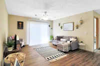 Inviting living room with cozy seating, modern decor, and a bright atmosphere from large windows and elegant blinds.