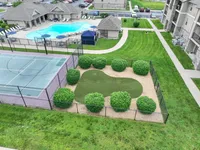 Inviting apartment complex with a sparkling swimming pool, modern tennis court, and lush green landscape, perfect for relaxation and recreation.