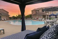 Luxurious poolside retreat with stylish lounge chairs and umbrellas under a vibrant sunset sky.