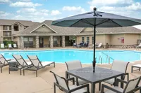 Inviting community pool area featuring relaxing lounge chairs, a stylish umbrella table, and scenic outdoor views, perfect for leisure and enjoyment.
