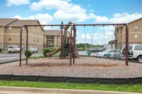 Charming playground area with swings and slide, set against welcoming apartment buildings and lush greenery.