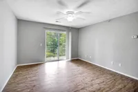 Bright and airy room with elegant wood flooring, ceiling fan, and a sliding door opening to a scenic balcony view.