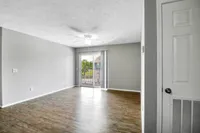 Bright, open living room with elegant wooden flooring, ceiling fan, and inviting balcony view.