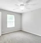 Bright and inviting bedroom with soft carpet flooring, a large sunlit window, and a modern ceiling fan.
