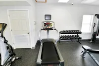 Modern fitness room featuring a treadmill, a set of free weights, and exercise equipment, offering a bright and inviting workout space.