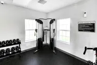 Brightly lit fitness room featuring sleek weight training equipment, modern dual cable machine, and convenient free weights for a comprehensive workout experience.