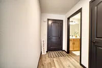 Welcoming apartment entrance featuring sleek dark doors, warm wood flooring, and a charming 'Happy Harvest' sign for a cozy aesthetic.