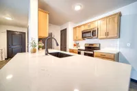 Modern kitchen boasting sleek white countertops, elegant wood cabinets, built-in stainless steel appliances, and stylish fixtures.