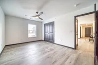 Bright and airy room with stylish wood flooring, modern ceiling fan, and elegant dark double doors offering a sleek and inviting ambiance.