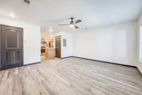 Sleek and modern living area with wood-inspired flooring, stylish ceiling fan, and open access to a contemporary kitchen with stainless steel appliances.