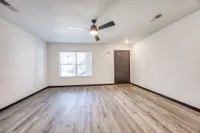 Bright living room with modern wood flooring, large window, and ceiling fan, ideal for cozy gatherings.