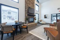 Contemporary living room with high ceiling, rustic stone fireplace, stylish seating area, and modern dining set, exuding warmth and elegance.