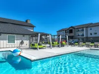 Luxurious apartment complex with refreshing swimming pool, stylish lounge chairs, and modern cabanas under a clear blue sky.