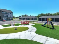 Charming community playground with vibrant green spaces and modern play equipment, surrounded by picturesque apartment buildings under a clear blue sky.