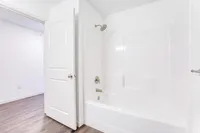 Modern bathroom with sleek white fixtures, a spacious bathtub-shower combo, and stylish wood flooring, perfect for relaxation.