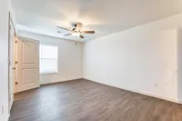Spacious and bright empty room with elegant wood flooring, modern ceiling fan, and large window for natural light.
