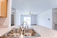 Modern open-plan living area with a sleek kitchen island, stainless steel sink, and bright natural light through sliding glass doors.