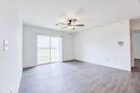 Bright and airy living room with elegant ceiling fan, sleek hardwood flooring, and expansive sliding glass doors leading to a serene outdoor view.
