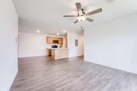 Bright and spacious open-concept living area with elegant wood flooring, modern ceiling fan, and a cozy kitchen featuring sleek appliances and wooden cabinetry.
