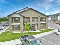 Modern two-story apartment building with ample parking spaces and well-maintained green lawn under a clear blue sky.