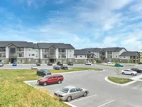 Modern apartment complex featuring spacious buildings with balconies, ample parking, and scenic views of a bright blue sky.