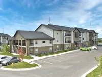 Modern apartment complex featuring spacious balconies, ample parking, and well-maintained landscaping under a bright blue sky.