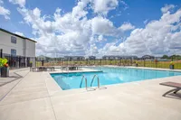 Inviting outdoor pool area with modern lounge chairs and vibrant planters, perfect for relaxation under a beautiful blue sky.