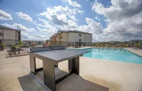Inviting outdoor pool area with modern lounge chairs and a ping pong table under a bright blue sky, perfect for relaxation and entertainment.