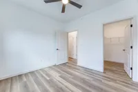 Bright bedroom with elegant wood flooring and ceiling fan, featuring two open doors leading to a spacious closet.