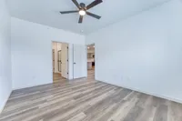 Bright and spacious room with modern wood flooring and ceiling fan, showcasing open doorways to kitchen and additional spaces.