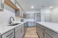 Modern kitchen with sleek gray cabinetry, marble countertops, and stainless steel appliances, featuring a spacious island and stylish subway tile backsplash.