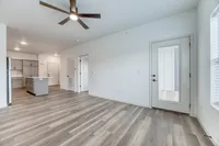 Bright and modern open-concept apartment showcasing sleek laminate flooring, a contemporary ceiling fan, and a spacious kitchen with stylish cabinetry.