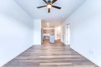 Modern open-concept apartment featuring sleek wood flooring, a stylish ceiling fan, and a spacious kitchen with stainless steel appliances.
