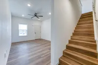 Bright and inviting entryway with modern wooden flooring, sleek ceiling fan, and elegant staircase leading to upper levels, perfect for a stylish living experience.