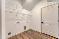 Bright utility room with modern wood flooring, featuring ample shelving and space for washer and dryer.