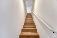 Inviting wooden staircase with sleek white walls offering a warm welcome to the upper levels of a modern home.