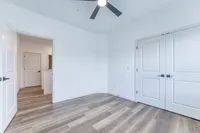 Bright and airy bedroom with sleek wood flooring and modern ceiling fan, offering ample space and stylish double doors.
