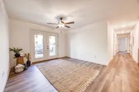 Bright and spacious living area with elegant hardwood floors, stylish ceiling fan, and double French doors leading to the outside.