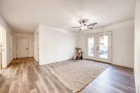 Inviting living area with elegant wood flooring, modern ceiling fan, and large glass doors leading to a sunlit patio.