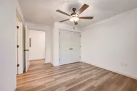 Bright and airy room featuring elegant wood flooring, a modern ceiling fan, and ample closet space, perfect for a cozy bedroom setup.
