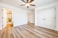 Bright, spacious bedroom with elegant wood flooring and a modern ceiling fan, leading to a stylish en-suite bathroom.