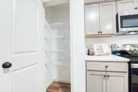 Bright kitchen corner with elegant cabinetry, modern appliances, and an open pantry, offering functional and stylish storage solutions.