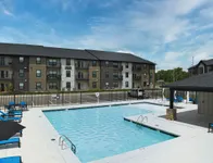Modern apartment complex with a sparkling outdoor pool, surrounded by sleek sun loungers and vibrant landscaping.