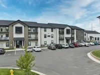 Modern apartment complex with spacious balconies, ample parking, and serene surroundings under a clear blue sky.