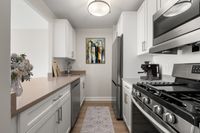 Sleek and modern kitchen with stainless steel appliances, stone countertops, six burner gas range, elegant white cabinetry, and stylish artwork, offering a perfect blend of functionality and design at Parkside Place, apartments in Cambridge, MA