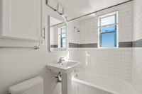 Bright and airy bathroom featuring modern white subway tiles, with a glass tile accent, a sleek pedestal sink, cabinetry for toiletries, and natural light