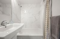 Elegant bathroom featuring a modern tiled bath surround and sleek pedestal sink